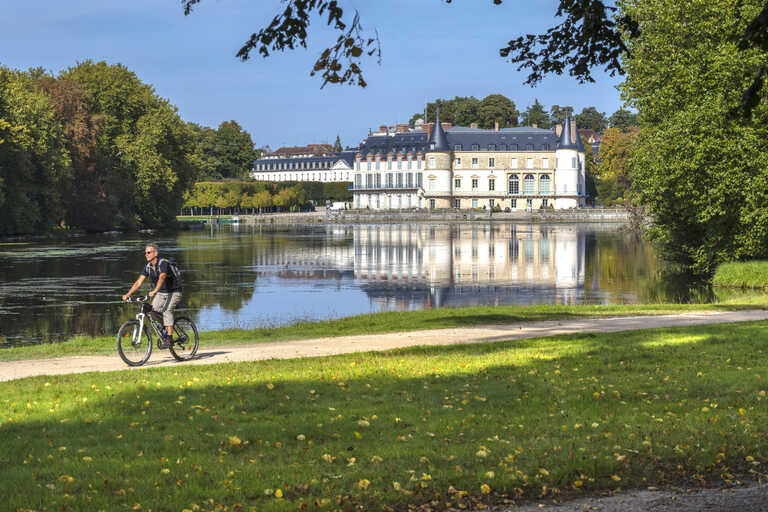homme faisant du vélo au bord d'un plan d'eau avec le chateau de Rambouillet derrière lui